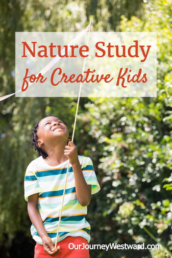 Boy with a green striped shirt and red shorts holds up a stick with a ribbon on top. For a blog post about nature study for creative kids.